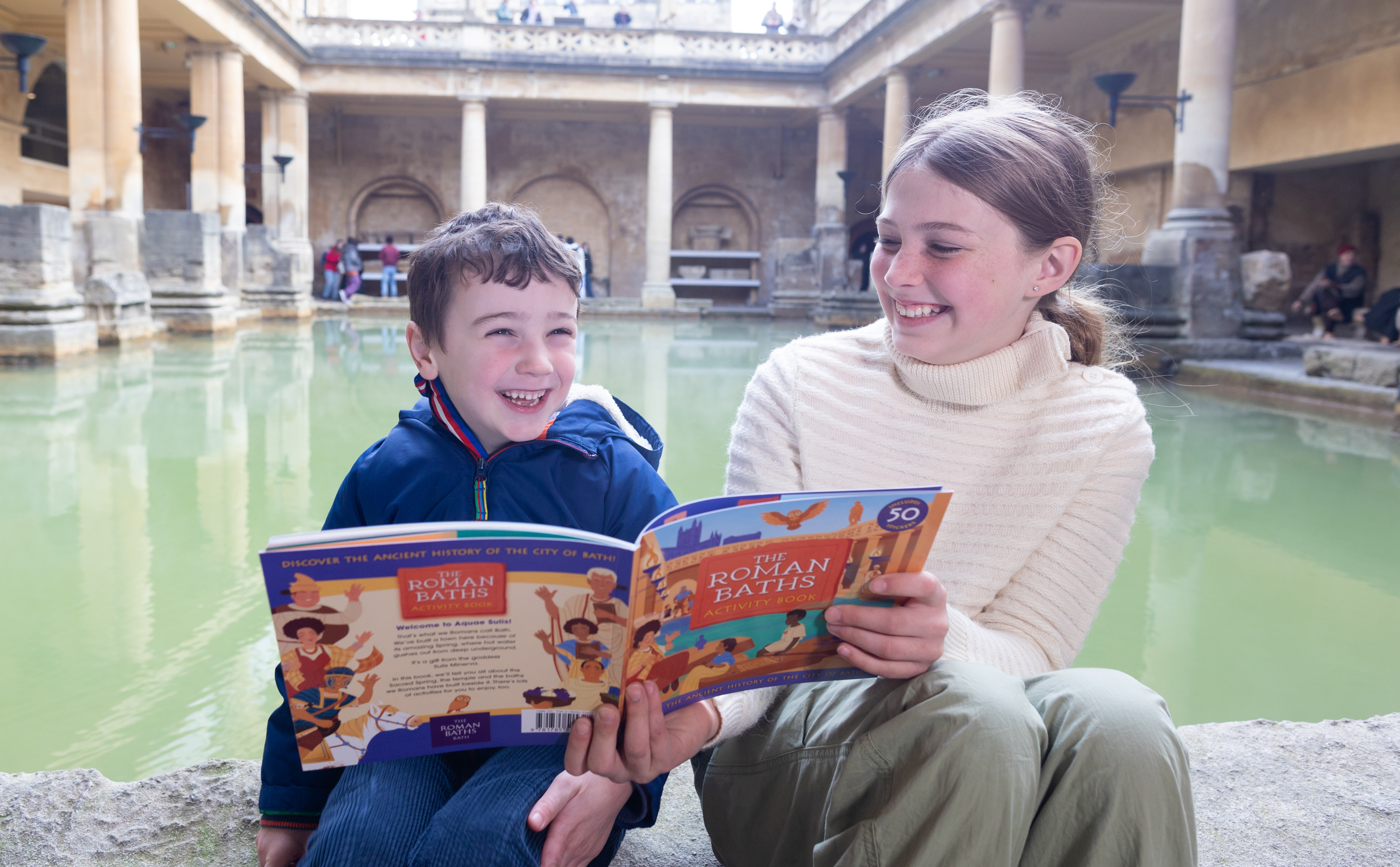 A boy and girl sitting by the Great Bath with a children's guidebook