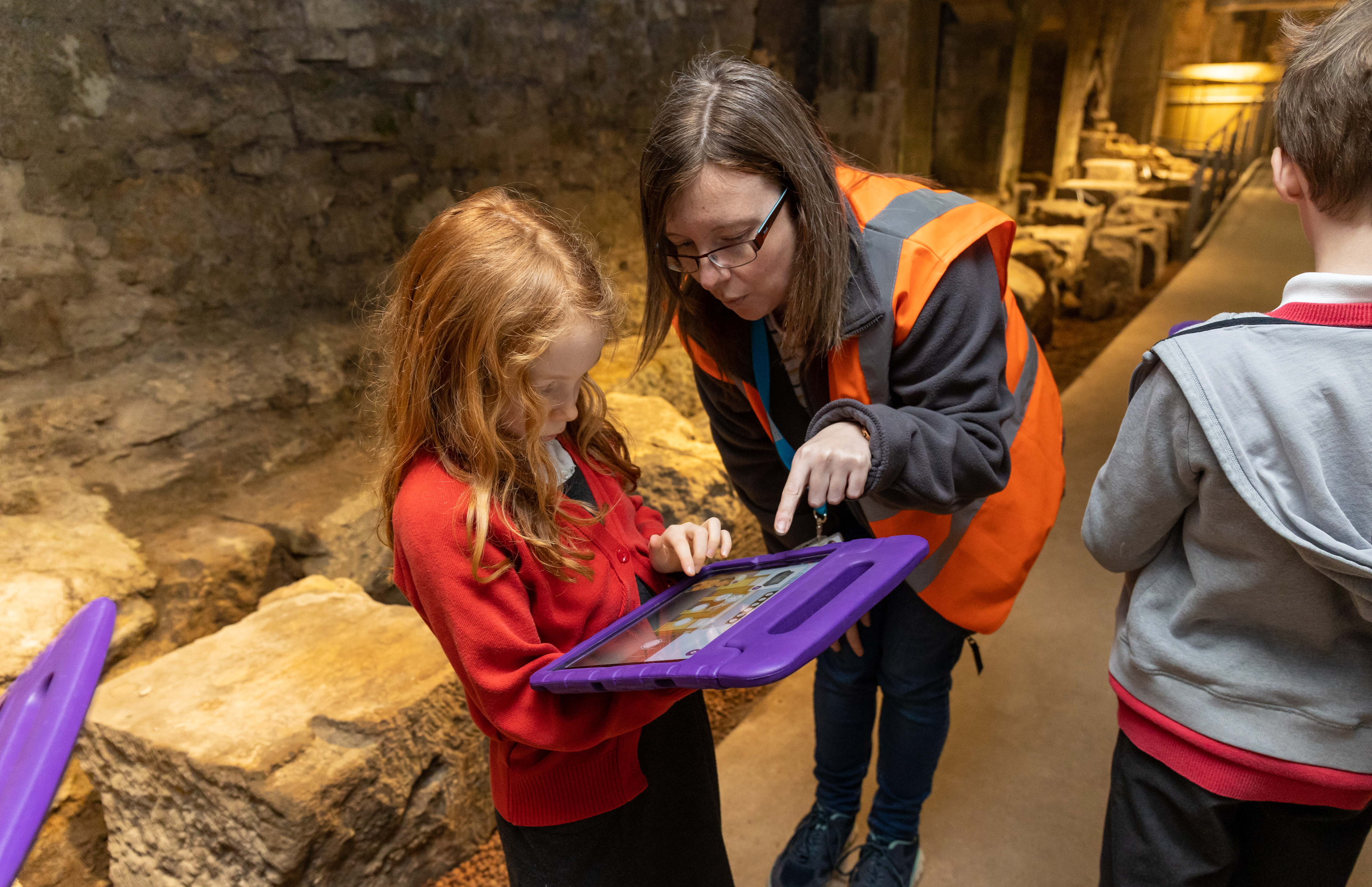 An adult helping a young schoolgirl with some work on a tablet, with stones in the background