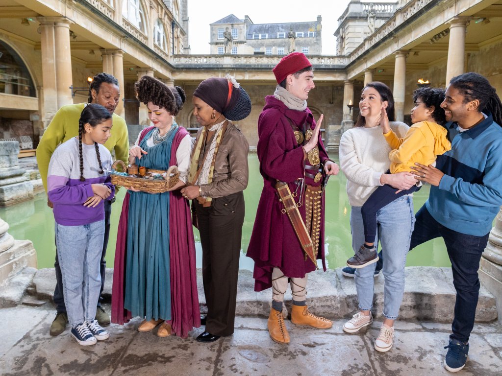 Image: A family interacting with costumed characters beside the Great Bath