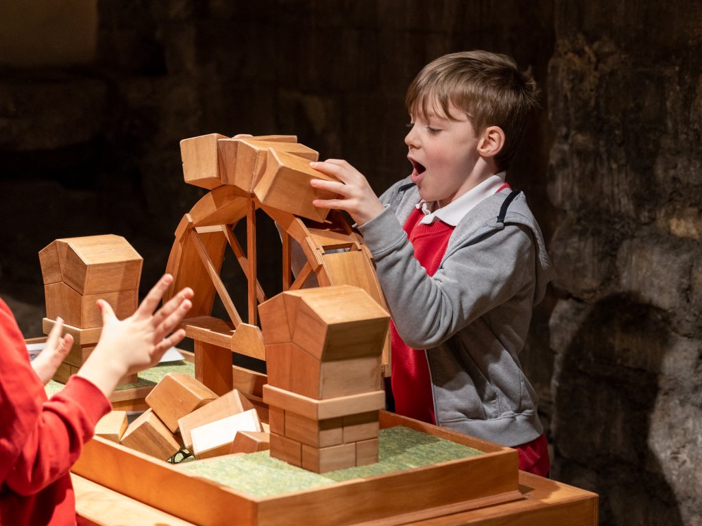 Image: A boy putting together a wooden arch. He has a surprised look on his face.