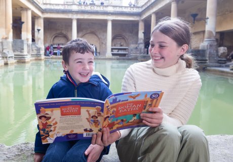 A boy and girl sitting by the Great Bath with a children's guidebook