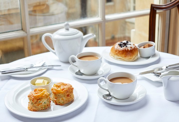 A table set with scones, a Bath bun and two cups of tea